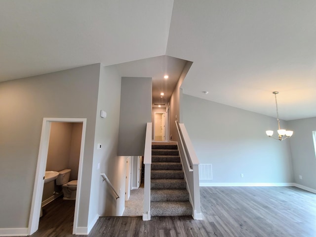 stairs featuring hardwood / wood-style floors, lofted ceiling, and an inviting chandelier