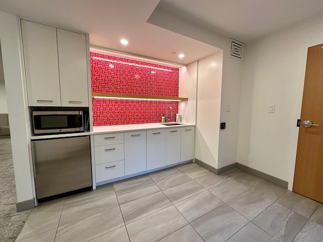 kitchen featuring decorative backsplash, light tile patterned floors, refrigerator, and sink