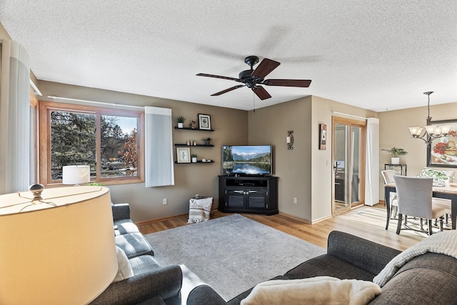 living room with ceiling fan with notable chandelier, light hardwood / wood-style flooring, and a textured ceiling