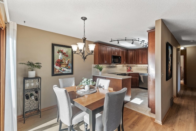 dining room with light hardwood / wood-style floors, a textured ceiling, and a notable chandelier