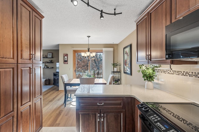 kitchen with black appliances, light hardwood / wood-style flooring, a notable chandelier, pendant lighting, and backsplash