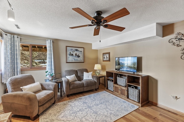 living room featuring ceiling fan, light hardwood / wood-style floors, and a textured ceiling