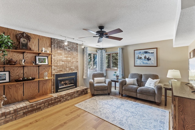 living room featuring hardwood / wood-style floors, rail lighting, a textured ceiling, and a brick fireplace