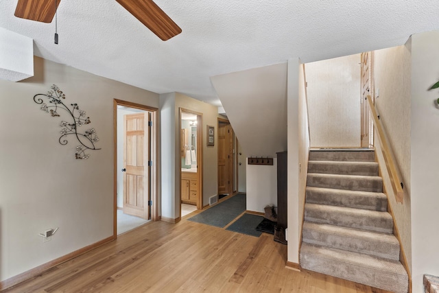 stairs featuring ceiling fan, wood-type flooring, and a textured ceiling