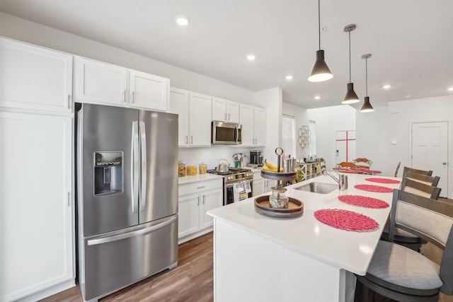 kitchen with stainless steel appliances, sink, decorative light fixtures, white cabinets, and an island with sink