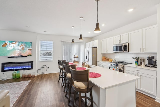 kitchen featuring white cabinets, decorative light fixtures, stainless steel appliances, and a center island with sink