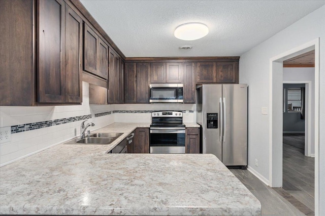 kitchen featuring appliances with stainless steel finishes, tasteful backsplash, dark brown cabinets, a textured ceiling, and sink