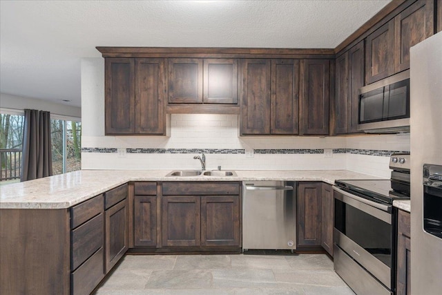 kitchen featuring dark brown cabinetry, light stone countertops, sink, kitchen peninsula, and appliances with stainless steel finishes