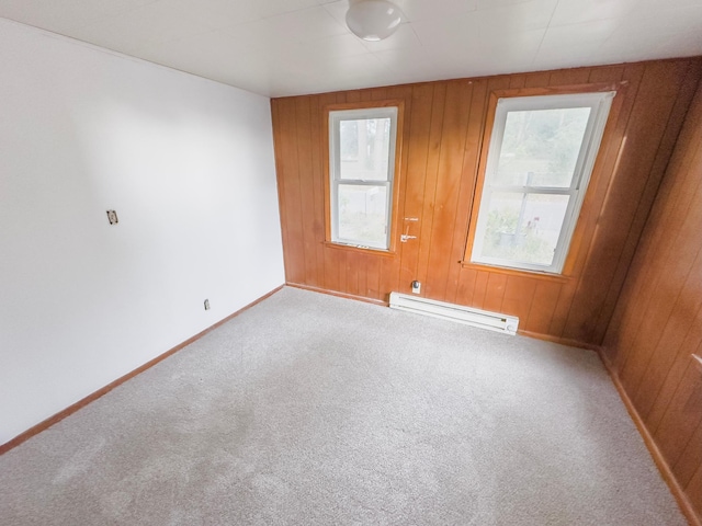 carpeted spare room featuring baseboard heating and wooden walls