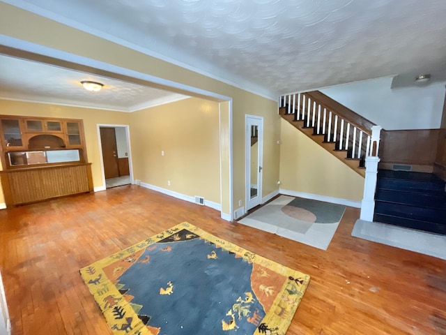 unfurnished living room with hardwood / wood-style floors, a textured ceiling, and ornamental molding