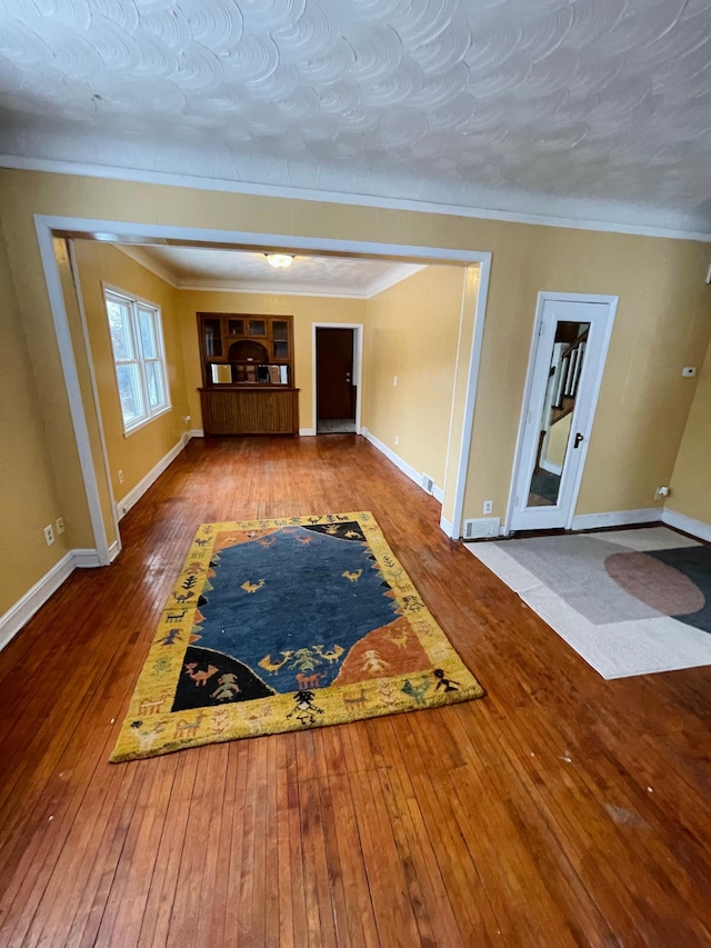 unfurnished living room with wood-type flooring, a textured ceiling, and ornamental molding