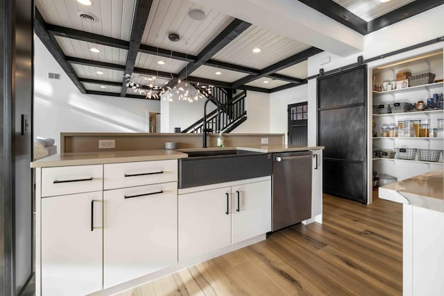 kitchen featuring beam ceiling, a barn door, dishwasher, and white cabinetry