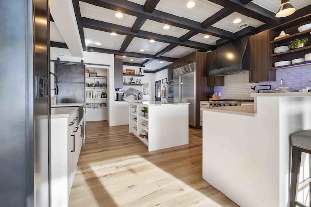 kitchen with appliances with stainless steel finishes, a kitchen island, premium range hood, a barn door, and coffered ceiling