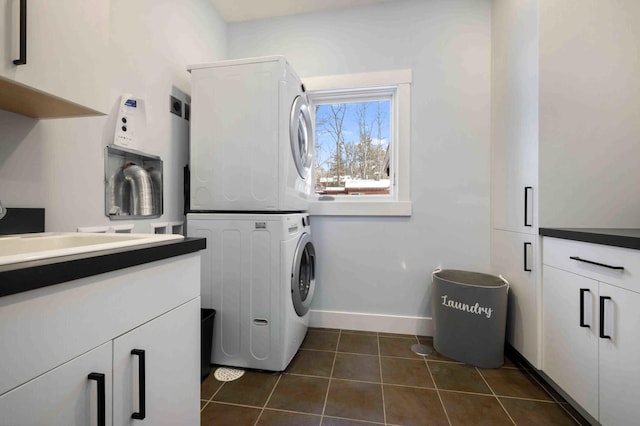 washroom featuring cabinets, stacked washer / drying machine, and dark tile patterned floors