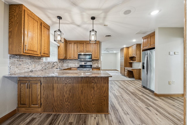 kitchen featuring kitchen peninsula, appliances with stainless steel finishes, light stone counters, sink, and hanging light fixtures