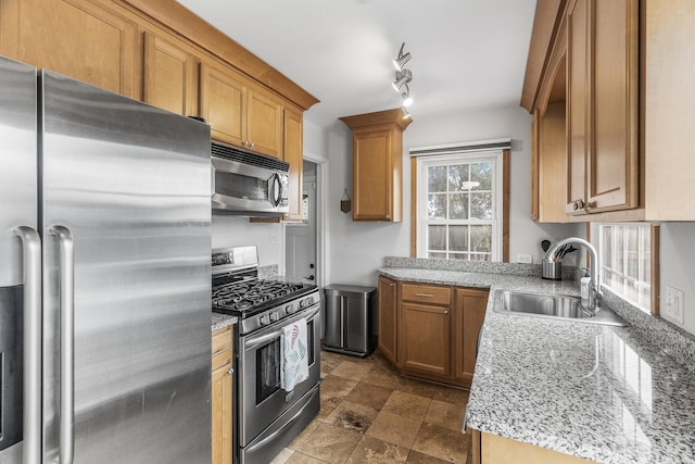 kitchen featuring brown cabinets, appliances with stainless steel finishes, stone finish flooring, a sink, and light stone countertops