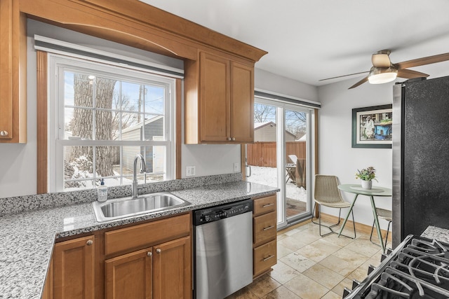 kitchen with ceiling fan, brown cabinets, light stone countertops, stainless steel appliances, and a sink