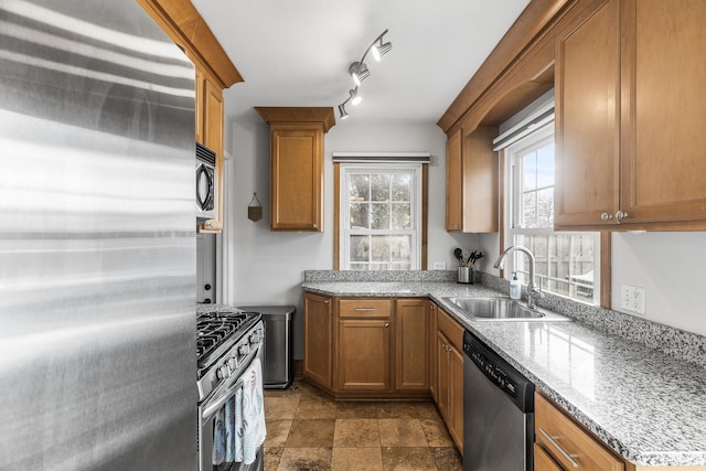 kitchen featuring stainless steel appliances, stone finish flooring, a sink, and brown cabinets