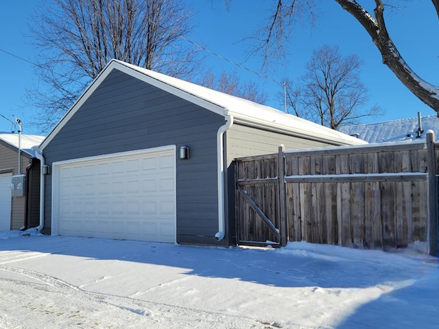 snow covered garage featuring a garage and fence