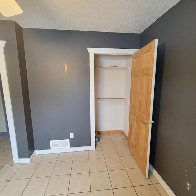 unfurnished bedroom featuring light tile patterned flooring, a textured ceiling, and a closet