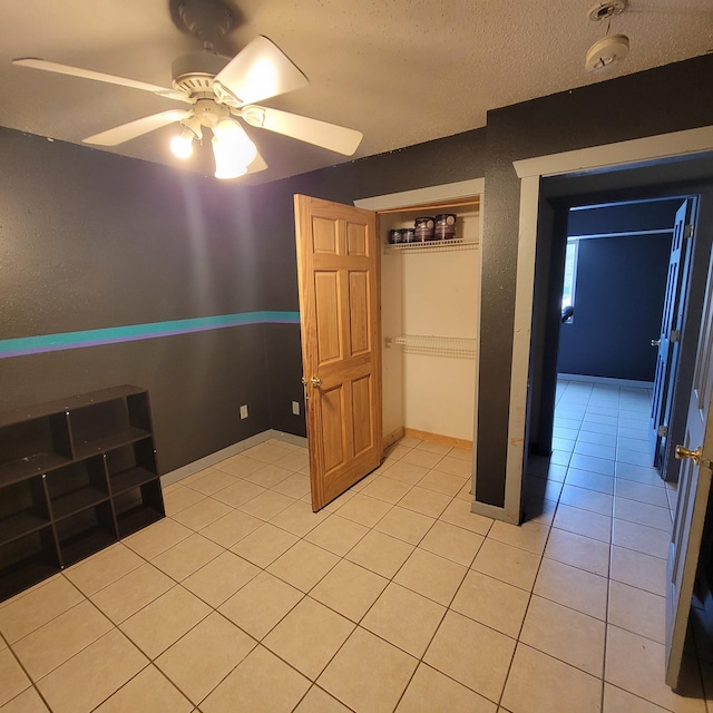 unfurnished bedroom featuring a textured ceiling, a closet, ceiling fan, and light tile patterned flooring