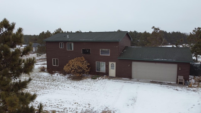 snow covered rear of property featuring log veneer siding and an attached garage