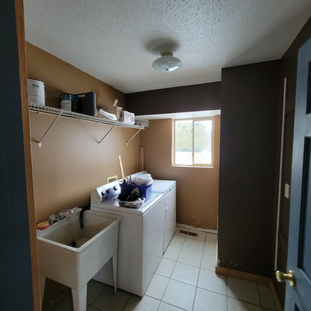 laundry area with light tile patterned flooring, a textured ceiling, washer and clothes dryer, and sink