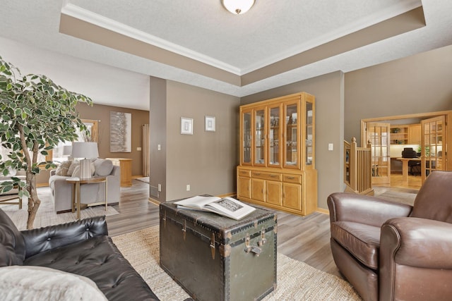 living room featuring light hardwood / wood-style flooring, ornamental molding, a raised ceiling, and a textured ceiling