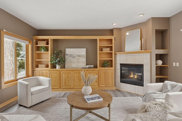 living room with a tiled fireplace, built in features, and light wood-type flooring