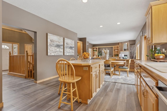 kitchen with light brown cabinets, light hardwood / wood-style flooring, a kitchen breakfast bar, and a kitchen island