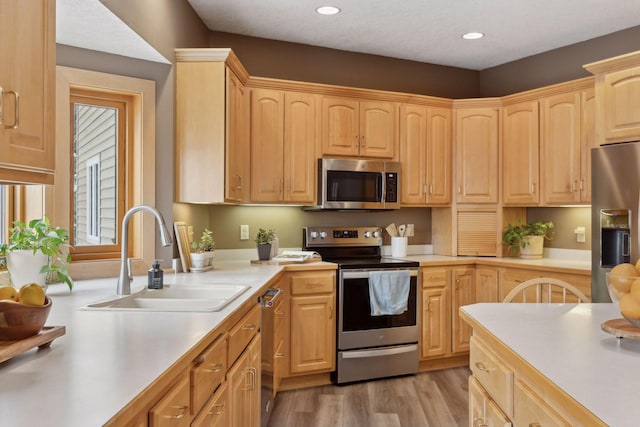 kitchen with appliances with stainless steel finishes, light hardwood / wood-style floors, sink, and light brown cabinets