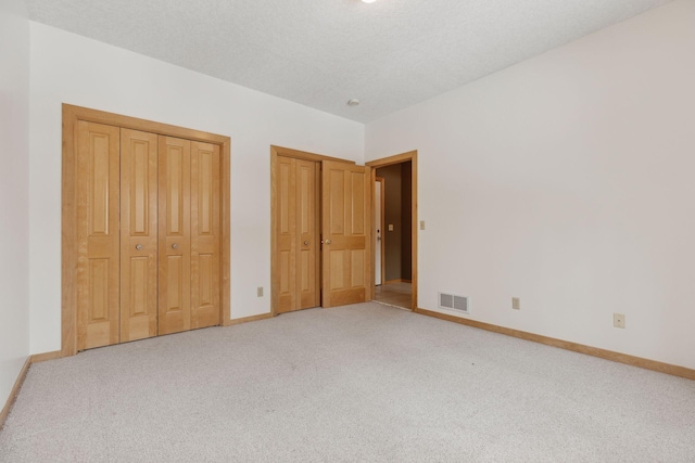 unfurnished bedroom with a textured ceiling, light carpet, and two closets