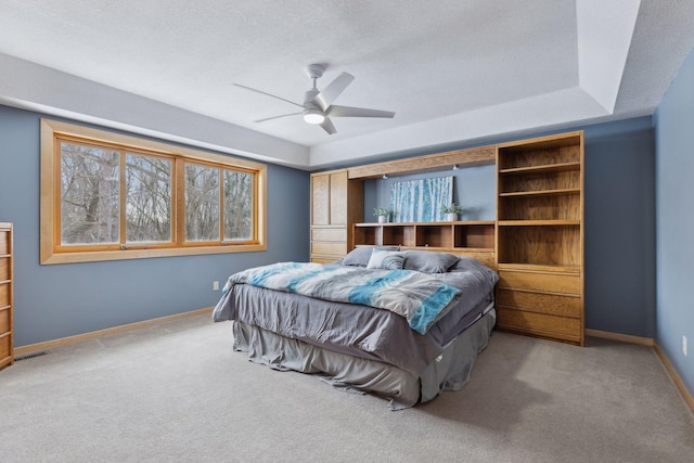 carpeted bedroom with ceiling fan, a tray ceiling, and a textured ceiling