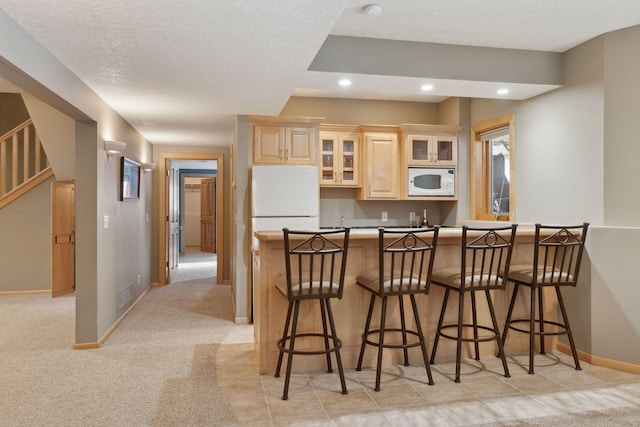 kitchen featuring a breakfast bar, white microwave, light brown cabinetry, kitchen peninsula, and a textured ceiling