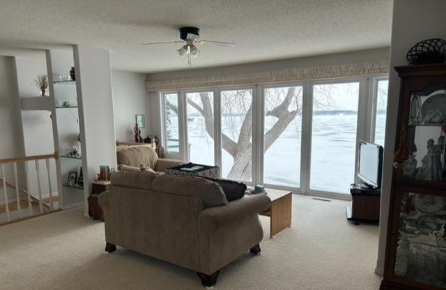 living room with a textured ceiling, light colored carpet, and ceiling fan