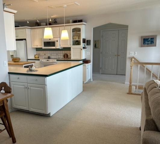 kitchen with tasteful backsplash, white appliances, a peninsula, decorative light fixtures, and light colored carpet
