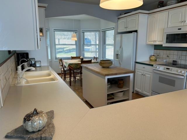 kitchen with white appliances, white cabinetry, a sink, and backsplash