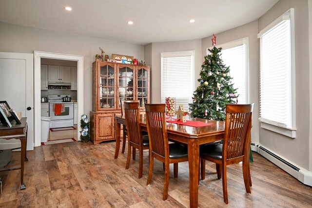 dining space featuring a healthy amount of sunlight, a baseboard heating unit, and hardwood / wood-style flooring