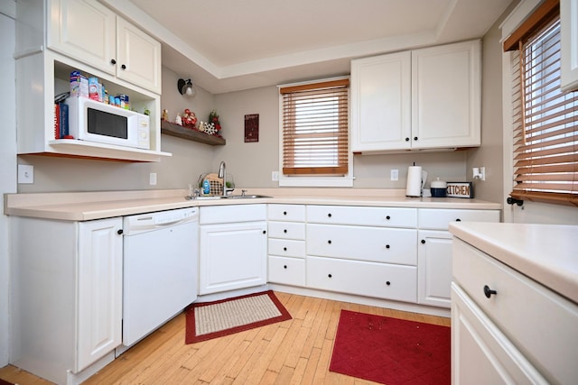 kitchen featuring white appliances, sink, light wood-type flooring, a tray ceiling, and white cabinetry