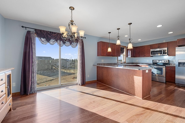 kitchen featuring pendant lighting, appliances with stainless steel finishes, kitchen peninsula, and a notable chandelier