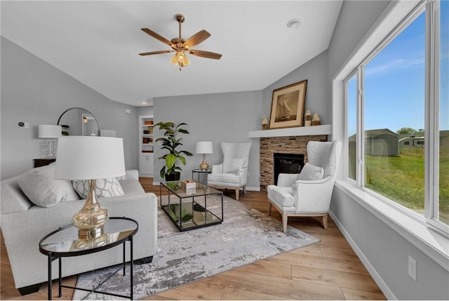 living room with a stone fireplace, ceiling fan, vaulted ceiling, and light wood-type flooring