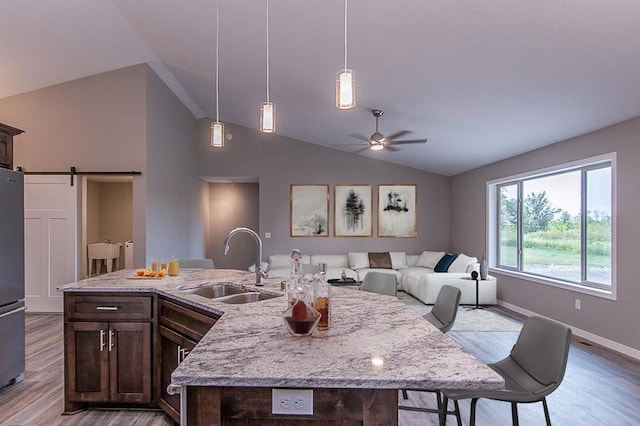 kitchen featuring sink, light hardwood / wood-style flooring, vaulted ceiling, a barn door, and light stone countertops