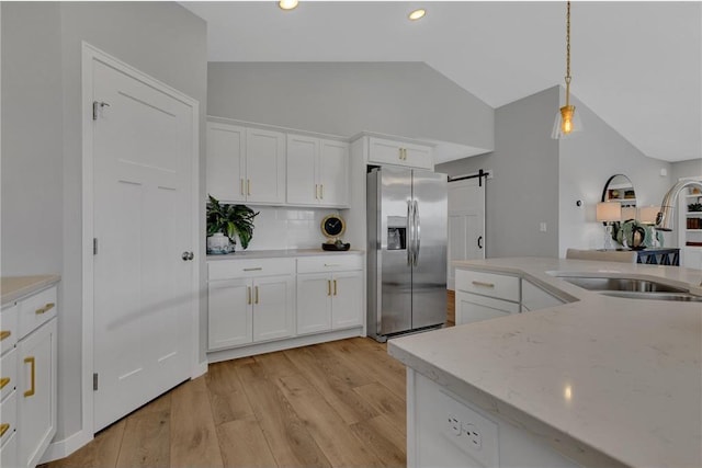 kitchen with pendant lighting, backsplash, white cabinets, stainless steel fridge, and a barn door