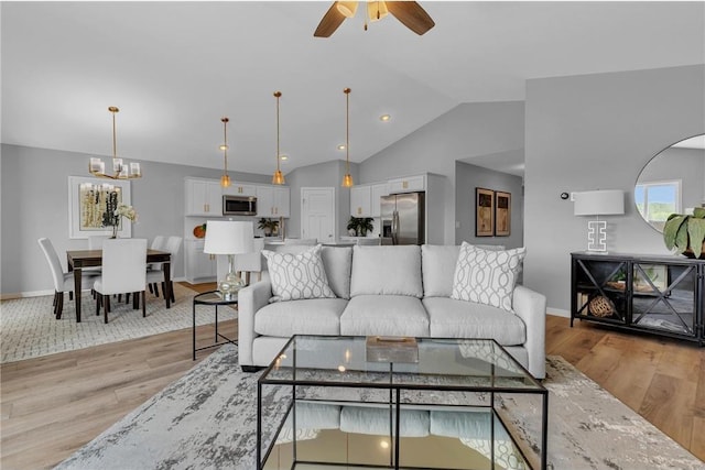 living room with light wood-type flooring, ceiling fan with notable chandelier, and lofted ceiling