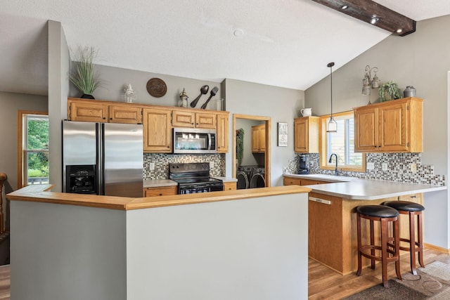 kitchen with stainless steel appliances, light hardwood / wood-style flooring, independent washer and dryer, decorative light fixtures, and a breakfast bar area