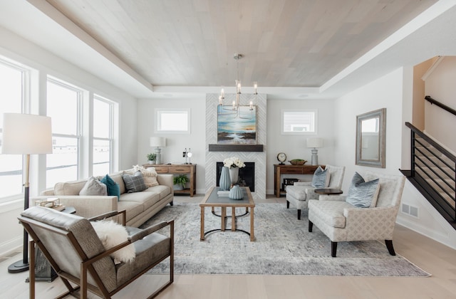 living room featuring a raised ceiling, a large fireplace, light hardwood / wood-style flooring, and a notable chandelier