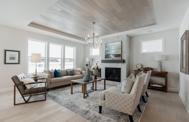 living room featuring a chandelier, light wood-type flooring, a tray ceiling, and a tiled fireplace