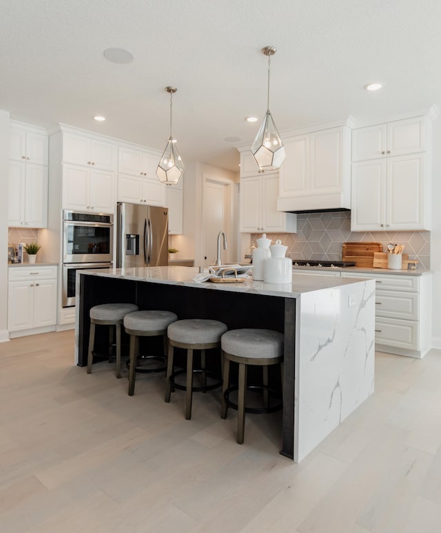 kitchen with white cabinets, a large island with sink, backsplash, and stainless steel appliances