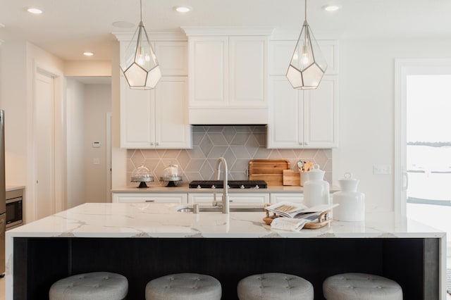 kitchen featuring decorative light fixtures, light stone countertops, and an island with sink