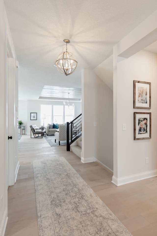 hall with light wood-type flooring and an inviting chandelier